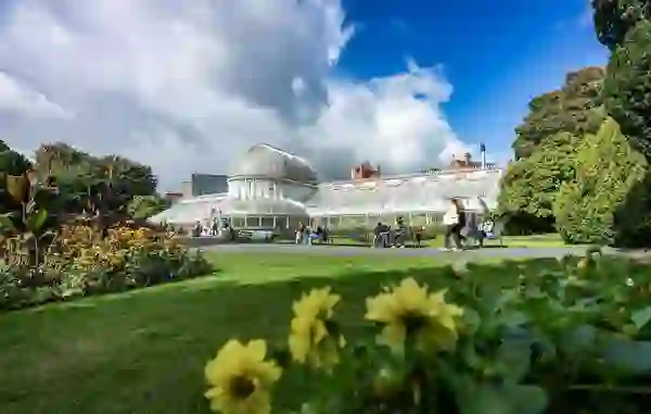 De Palm House-kas in de Botanic Gardens van Belfast, omringd door grasvelden, bloemen en bezoekers.