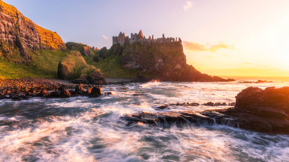 Dunluce Castle boven de beukende golven aan de Causeway kust bij zonsondergang, county Antrim.