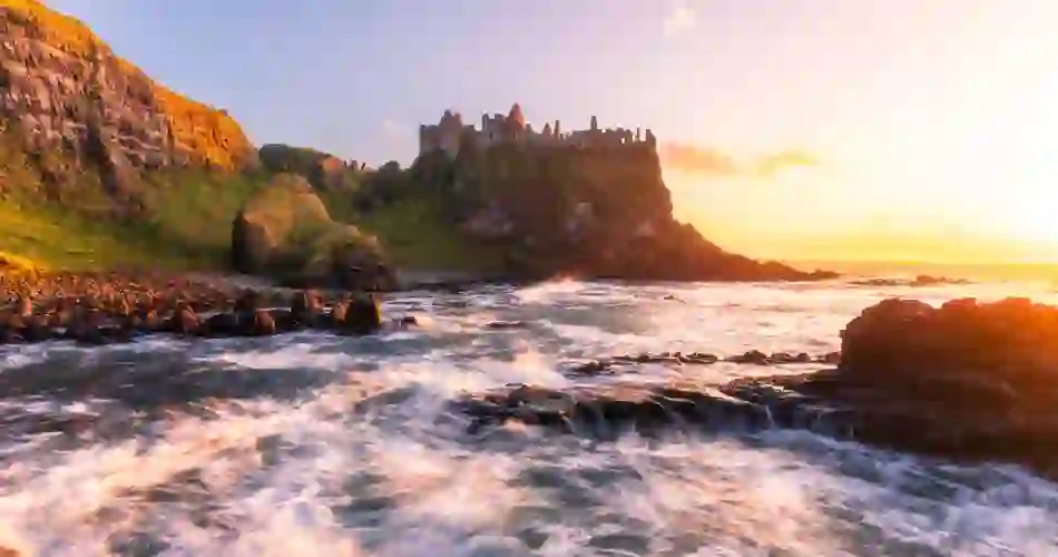 Dunluce Castle boven de beukende golven aan de Causeway kust bij zonsondergang, county Antrim.