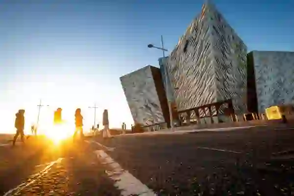 Mensen die bij zonsondergang langs Titanic Belfast lopen in het Titanic Quarter.