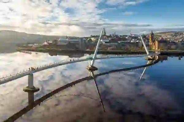 De Peace Bridge weerspiegeld in de rivier de Foyle, met op de achtergrond de skyline van Derry~Londonderry.