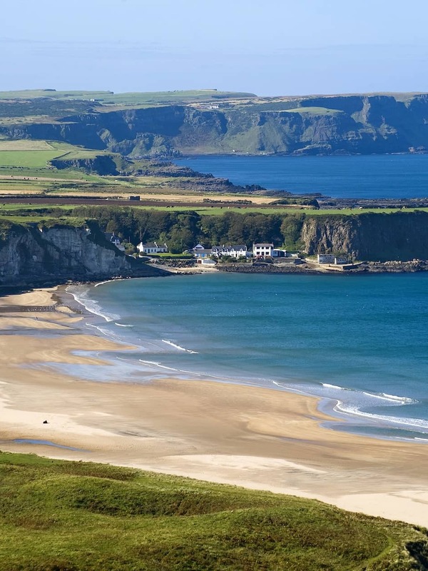 Panoramablick auf die Whitepark Bay mit türkisfarbenem Meer und weißen Cottages unterhalb der Klippen, Grafschaft Antrim.