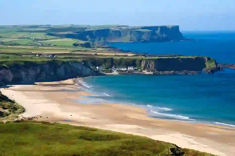 Een panoramisch uitzicht op Whitepark Bay met turquoise zee en witte huisjes genesteld onder de kliffen, county Antrim.