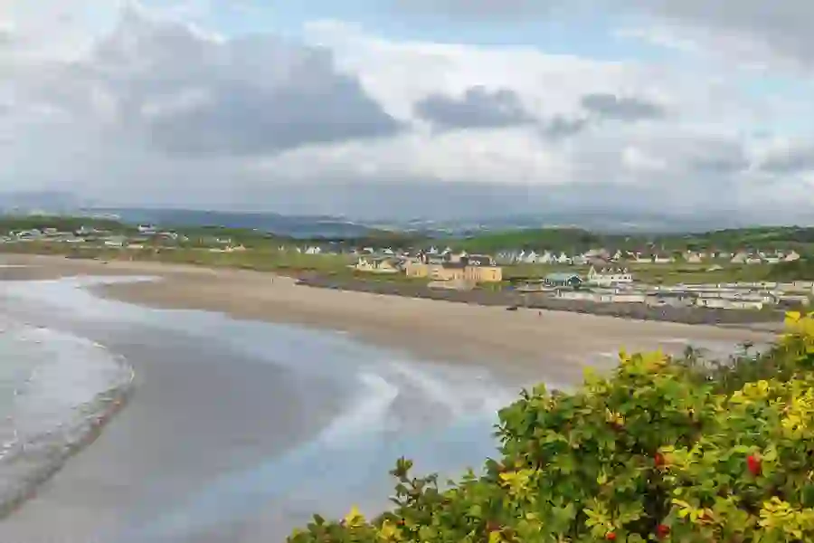 Weidse blik op Rossnowlagh Beach in county Donegal, met zacht zand en kusthuizen verscholen tussen groene heuvels.