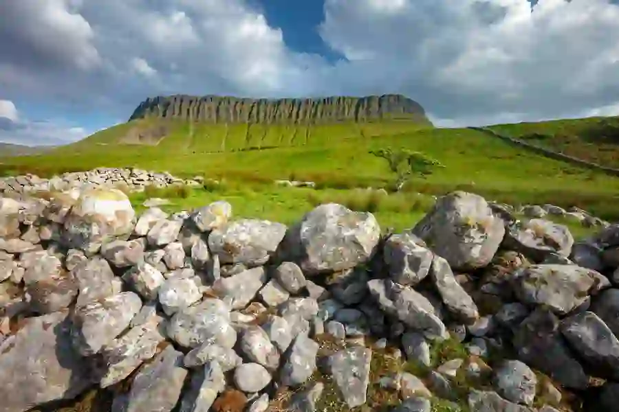 De berg Ben Bulben in county Sligo torent boven groene velden en een traditionele, droge stenen muur onder een prachtige lucht.