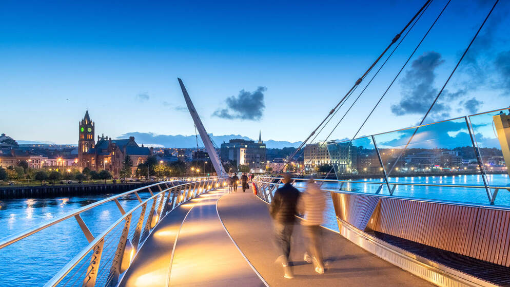 Peace Bridge at dusk with Guildhall clock tower in Derry~Londonderry city centre.