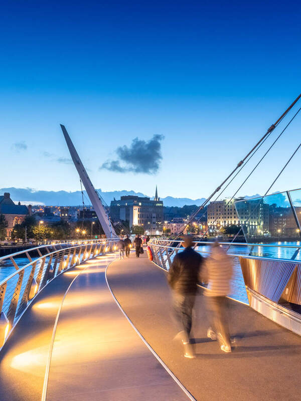Peace Bridge al tramonto con la torre dell'orologio del municipio nel centro della città di Derry~Londonderry.