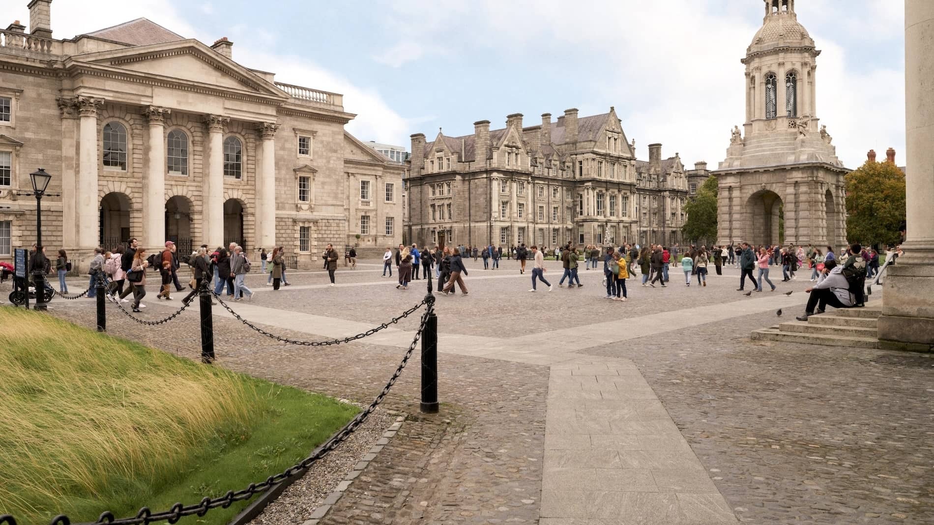 Studenten und Besucher schlendern über den gepflasterten Vorplatz des Trinity College Dublin, mit dem Campanile und historischen Gebäuden.