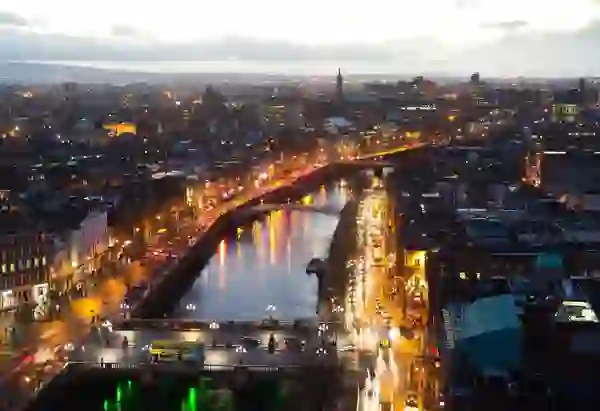 Luftaufnahme des Flusses Liffey bei Nacht - mit Brücken, Verkehr und Lichtern der Stadt; das Stadtzentrum von Dublin und das Custom House sind beleuchtet.