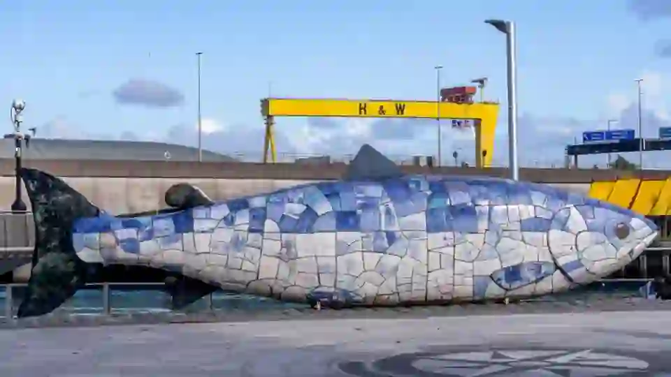 Die Skulptur „Salmon of Knowledge“ am Donegall Quay in Belfast mit dem Kran von Harland und Wolff im Hintergrund.