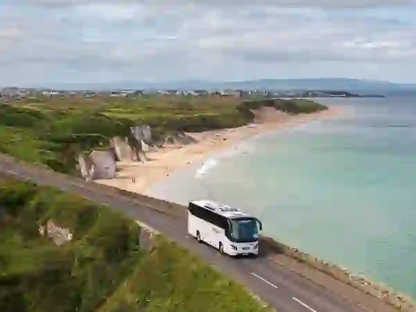 Ein Reisebus fährt entlang der Antrim Coast Road oberhalb eines Sandstrandes nahe Portrush.