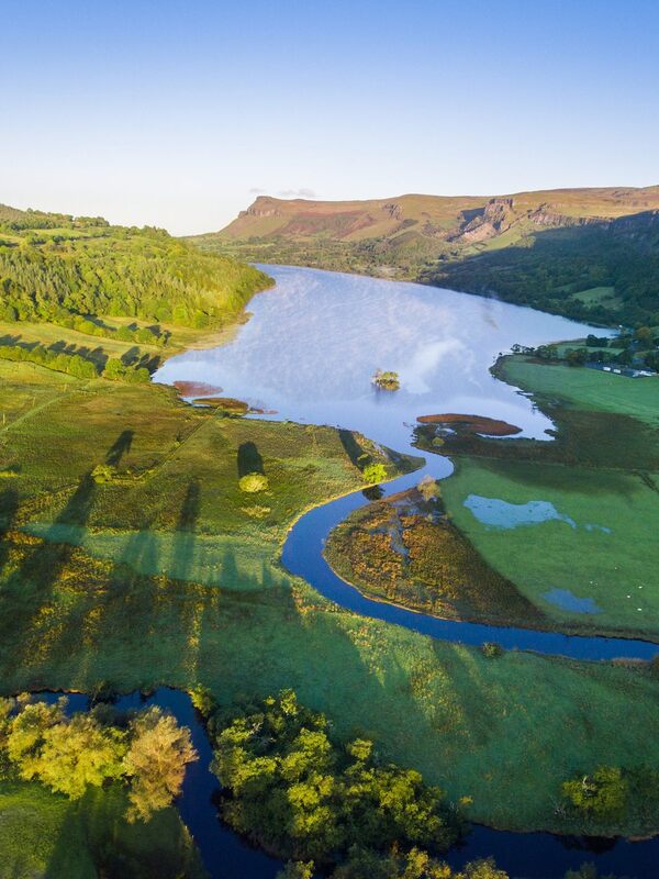 Vue aérienne de la campagne de Bundoran avec une rivière qui se jette dans un lac entouré de champs verts et de bois.