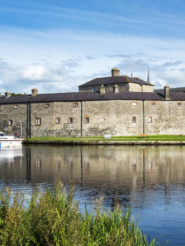 Rovine di una chiesa di pietra con un portale ad arco e una torre rotonda sull'isola di Devenish, presso Lough Erne, sotto un cielo blu con le nuvole.