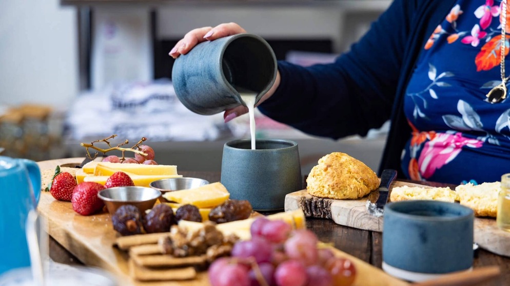 Close-up of milk poured into a cup beside cheese, grapes and a scone on a table in Ireland’s Hidden Heartlands.