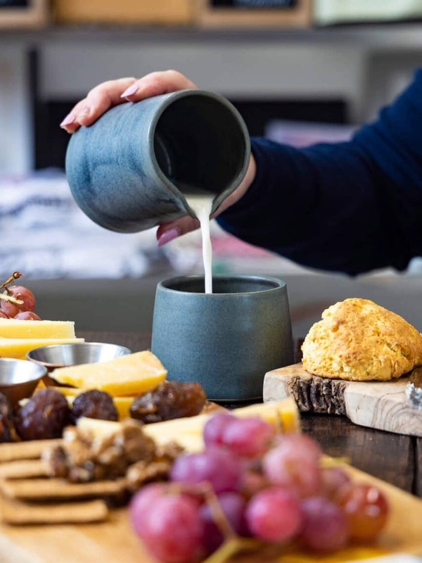 Close-up of milk poured into a cup beside cheese, grapes and a scone on a table in Ireland’s Hidden Heartlands.