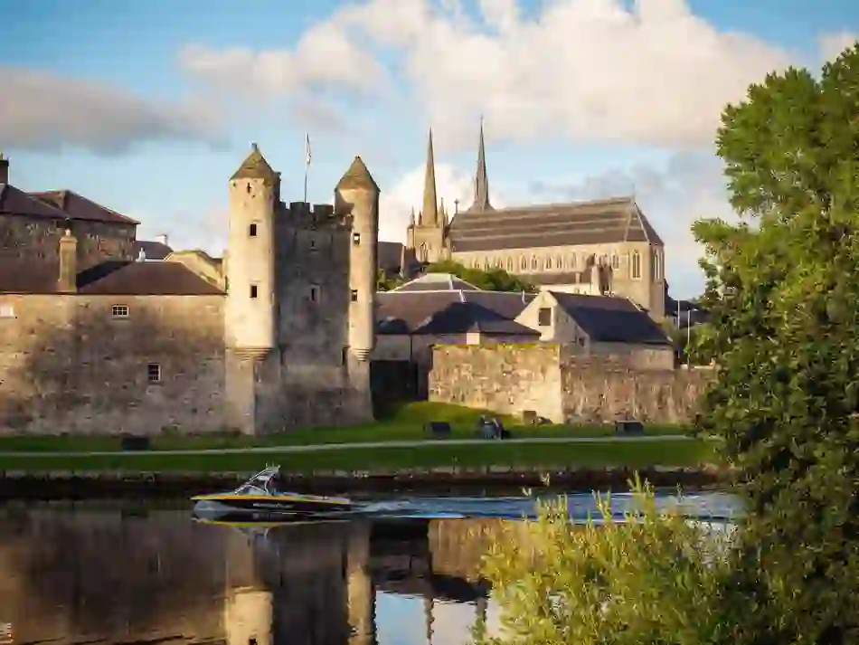 Bateau à moteur passant devant le château d'Enniskillen sur la rivière Erne, avec la cathédrale St Macartin s'élevant derrière.