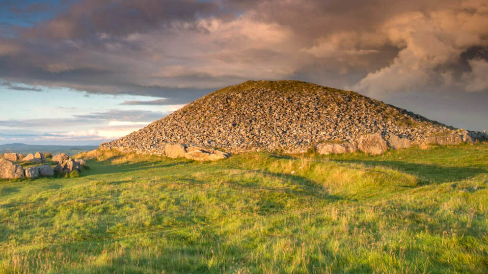 Tumulo di pietra antico presso le tombe di passaggio di Loughcrew sotto un cielo serale drammatico.