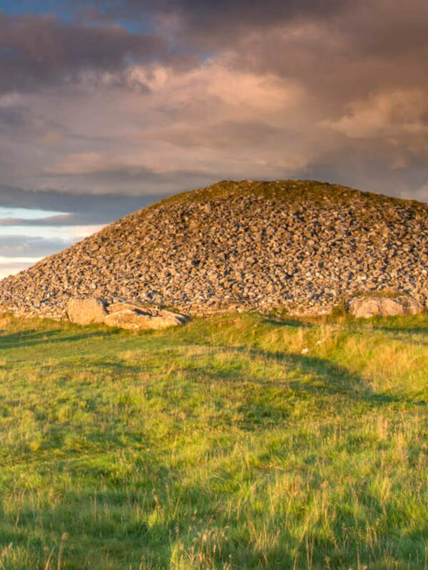Tumulo di pietra antico presso le tombe di passaggio di Loughcrew sotto un cielo serale drammatico.