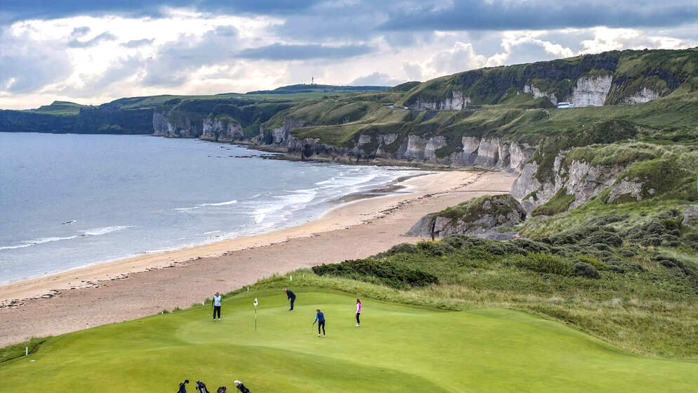 Golfers die spelen bij de Royal Portrush Golf Club met zeekliffen op de achtergrond.
