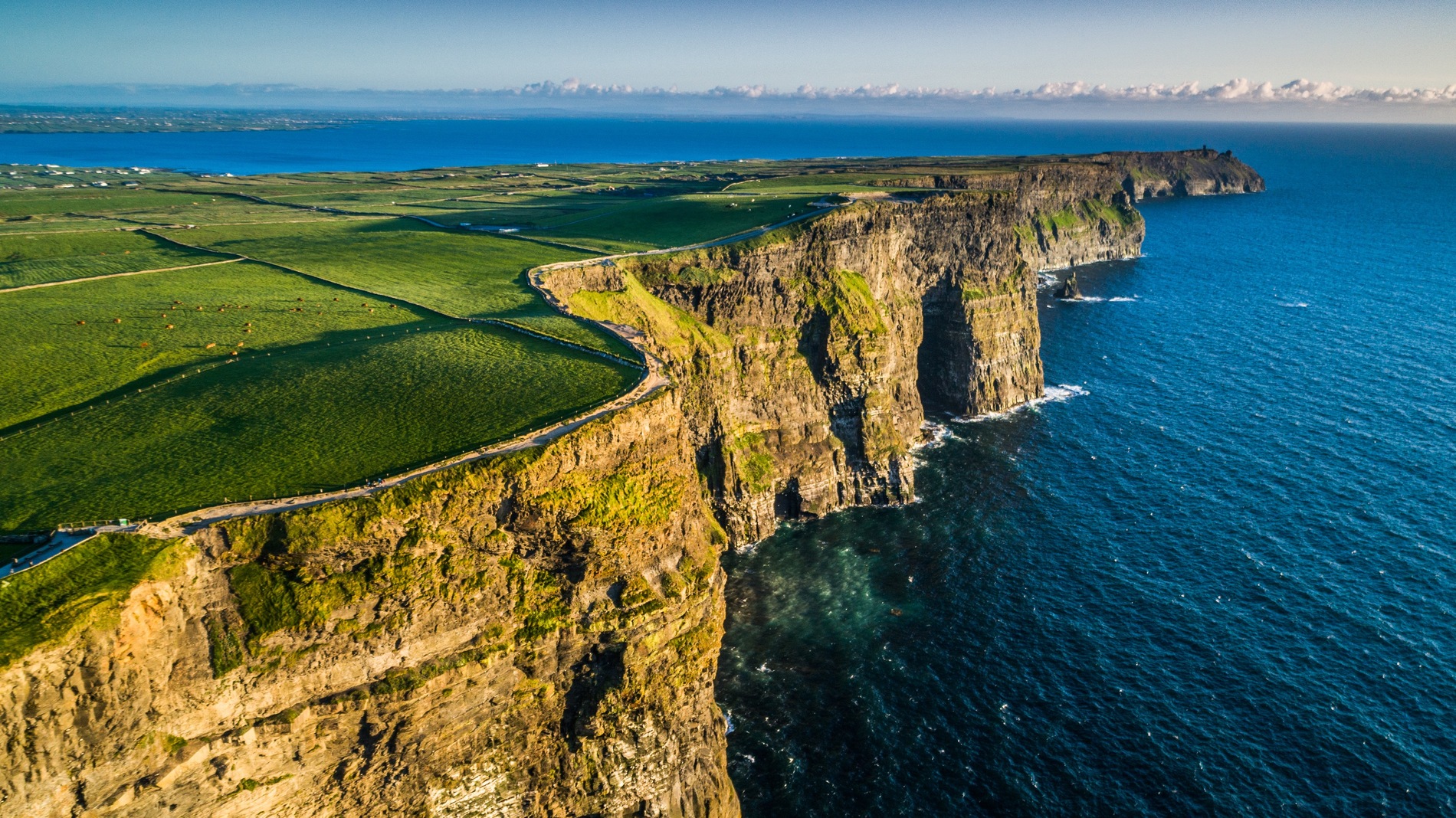 Vista aérea de los acantilados de Moher con vistas al océano Atlántico en el condado de Clare, con campos que se extienden tierra adentro.