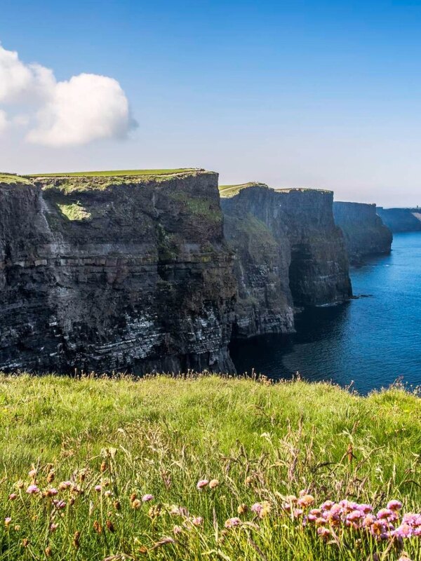 Cliffs of Moher rising above the Atlantic Ocean under a bright blue sky in County Clare.