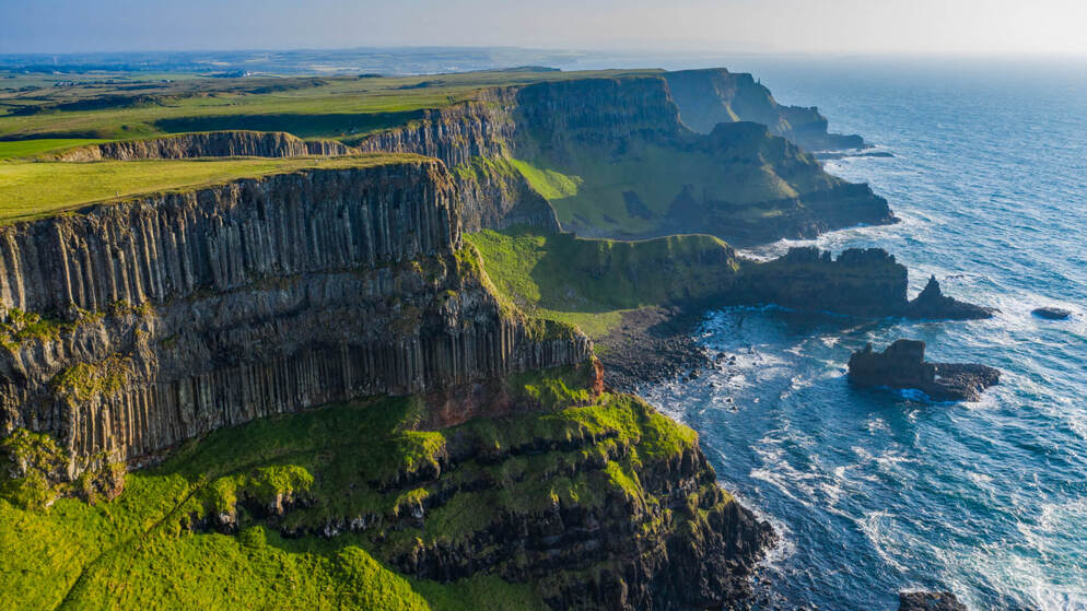 Basalt cliffs along the wild northern coast of Ireland at sunset, with waves crashing below.