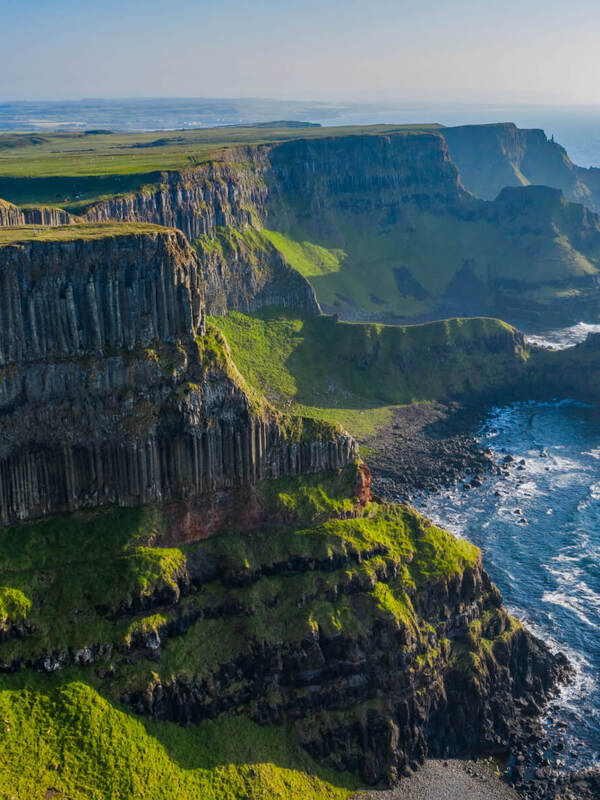 Basaltklippen entlang der wilden NordKüste von Irland bei Sonnenuntergang, mit brechenden Wellen darunter.