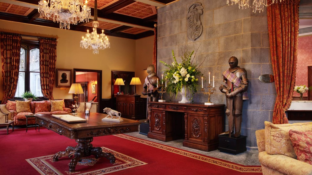 Grand castle hotel interior with chandeliers, antique furniture, floral display and two suits of armour.