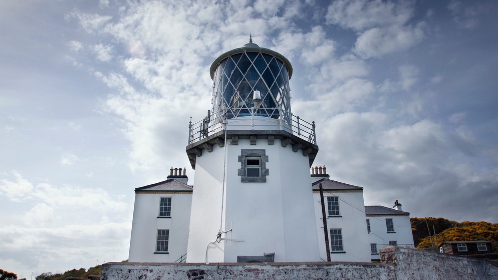Historic Irish lighthouse, Blackhead Lighthouse in County Antrim beneath a dramatic, cloud-filled sky.