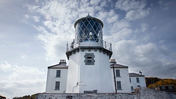 Historic Irish lighthouse, Blackhead Lighthouse in County Antrim beneath a dramatic, cloud-filled sky.