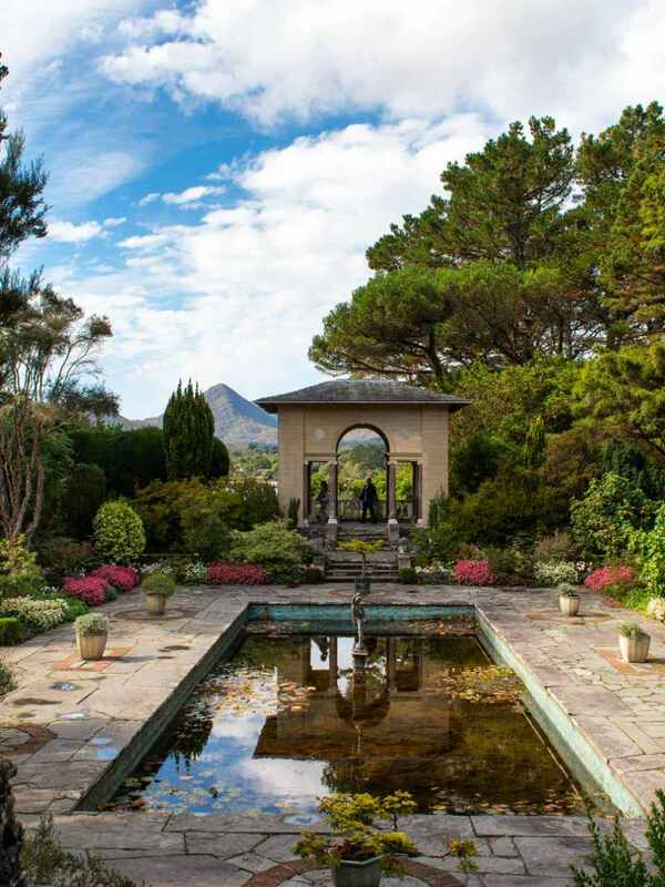 Grand entrance of Wells House framed by trees and gardens, under a partly cloudy sky in County Wexford.