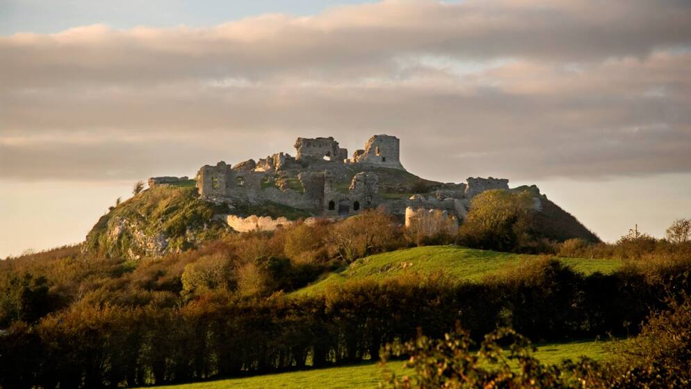 Ruins of a hilltop fortress bathed in golden light at sunset on the Rock of Dunamase in Ireland’s Ancient East.