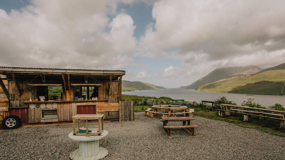 Rustic wooden food stall with picnic benches overlooking a scenic lake and mountains in County Galway.