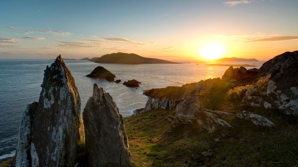 Puesta de sol sobre las Islas Blasket, vista desde un cabo rocoso en la península de Dingle, con imponentes formaciones rocosas en silueta.