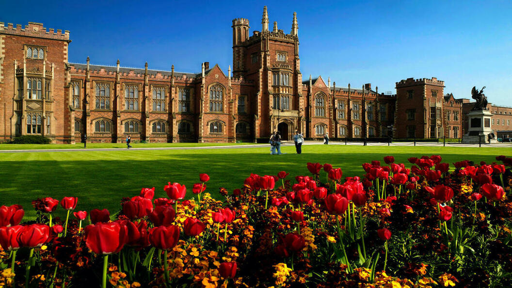 Das Gebäude der Queen's University Belfast hinter Frühlingstulpen und Rasenflächen unter strahlend blauem Himmel.