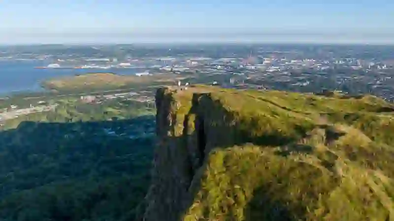Aussichtspunkt auf dem Cave Hill mit Blick auf die Stadt Belfast und den Belfast Lough. Am Rand stehen Wanderer.
