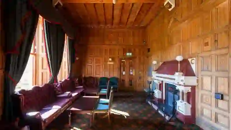 Ein holzvertäfeltes Wohnzimmer im Belfast Castle mit einem kunstvollen Kamin, Ledersofas und hohen Fenstern mit Blick auf das Gelände.