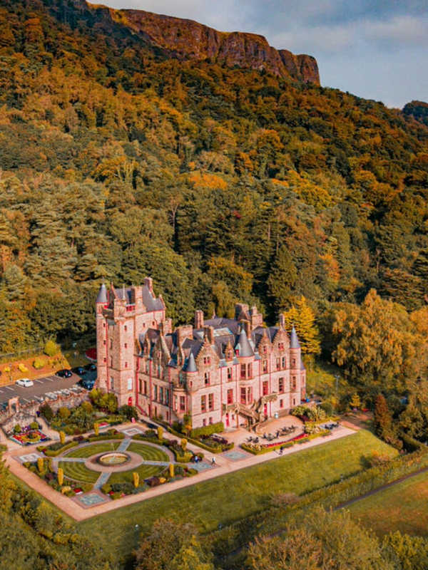 Belfast Castle nestled in autumn woodland on the slopes of Cave Hill, glowing in warm sunset light above the Belfast landscape.