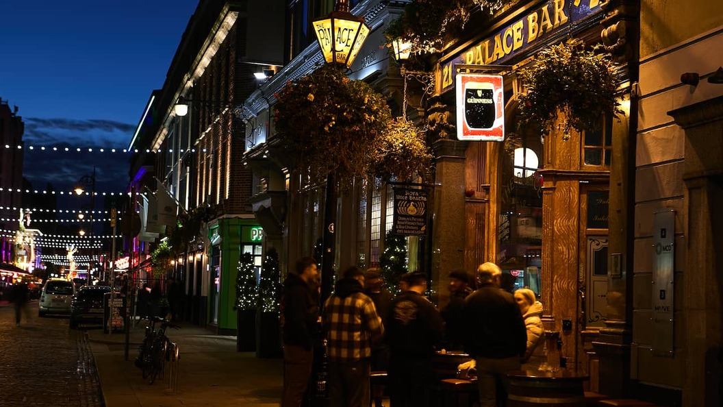 The Palace Bar on Fleet Street in Dublin at night, glowing with warm lights and outdoor tables.