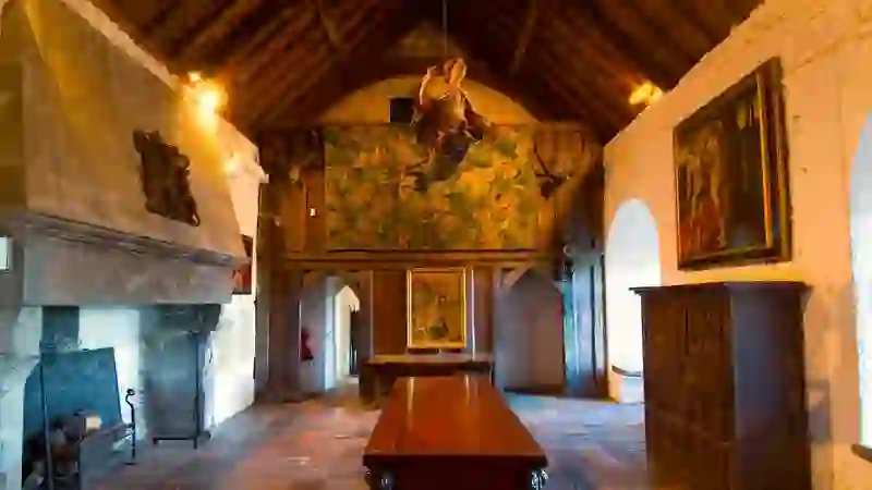 Interior of Bunratty Castle’s Great Hall, featuring a long wooden table, stone fireplace and medieval artwork.