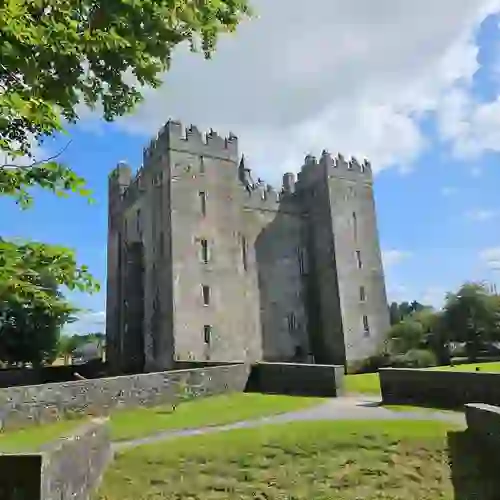 Bunratty Castle in County Clare, surrounded by green lawns and trees under a blue sky.