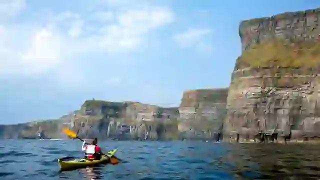 Kayaker paddling beneath the Cliffs of Moher on the Atlantic Ocean, with towering limestone cliffs in the background.