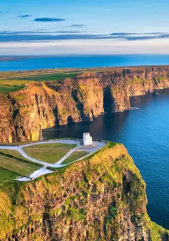 Aerial sunrise view of the Cliffs of Moher with O’Brien’s Tower perched above the Atlantic along the County Clare coastline.