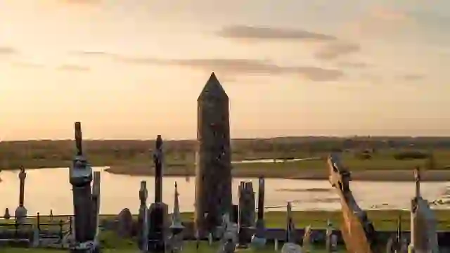 De ronde toren en begraafplaats van Clonmacnoise bij zonsondergang met uitzicht op de rivier Shannon in county Offaly.