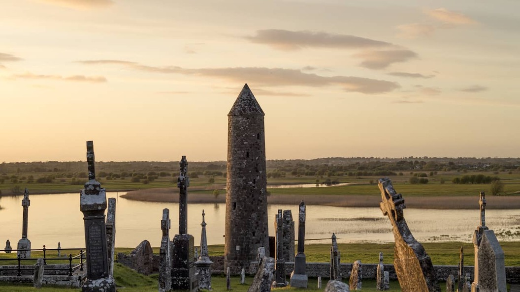 De ronde toren en begraafplaats van Clonmacnoise bij zonsondergang met uitzicht op de rivier Shannon in county Offaly.