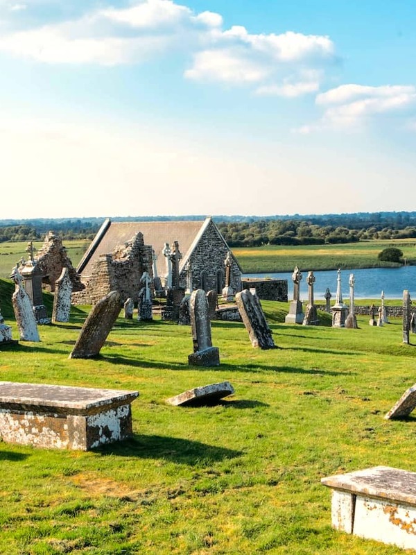 Grabsteine ​​und Kirchenruine in Clonmacnoise mit Blick auf den Fluss Shannon in der Grafschaft Offaly.