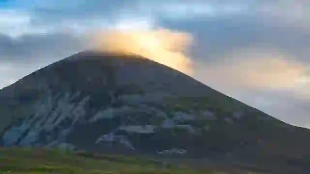 Der Berg Croagh Patrick bei Sonnenuntergang, mit goldenem Licht, das durch die Wolken über dem Gipfel in der Grafschaft Mayo, Irland, bricht.