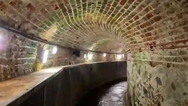 Brick-lined tunnel inside Crumlin Road Gaol, Belfast, with curved walls, damp floor and strip lighting.