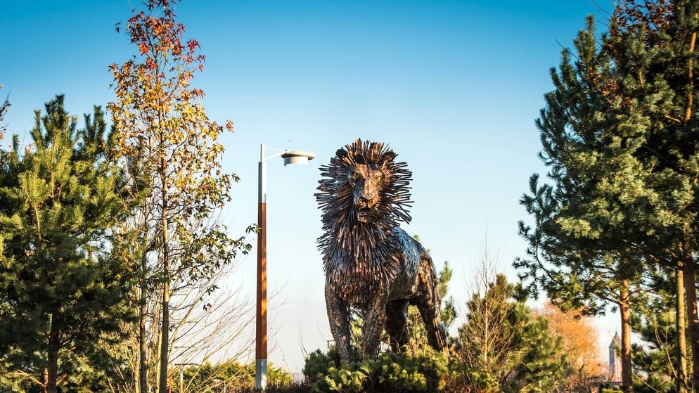 Large metal Aslan lion sculpture among trees at CS Lewis Square in Belfast.