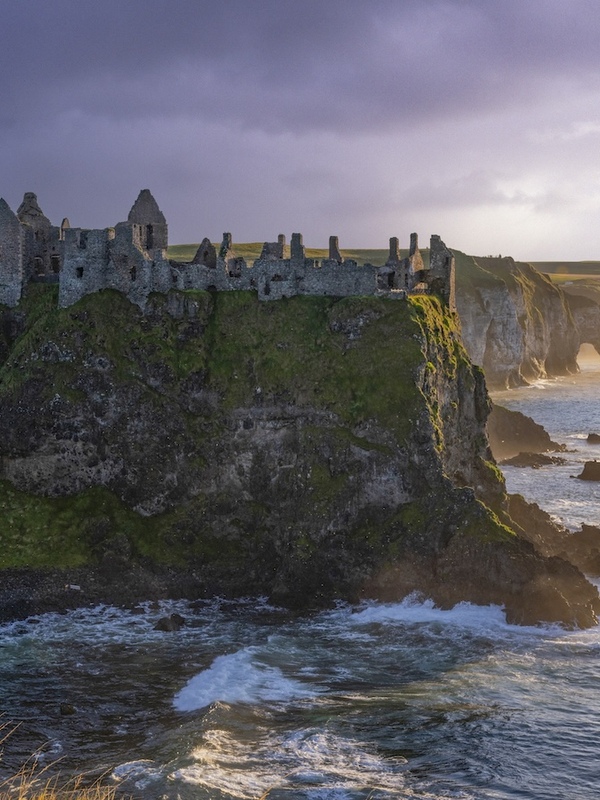 Die Ruinen von Dunluce Castle thronen im Sonnenuntergang auf den spektakulären Klippen entlang der Causeway Coast.